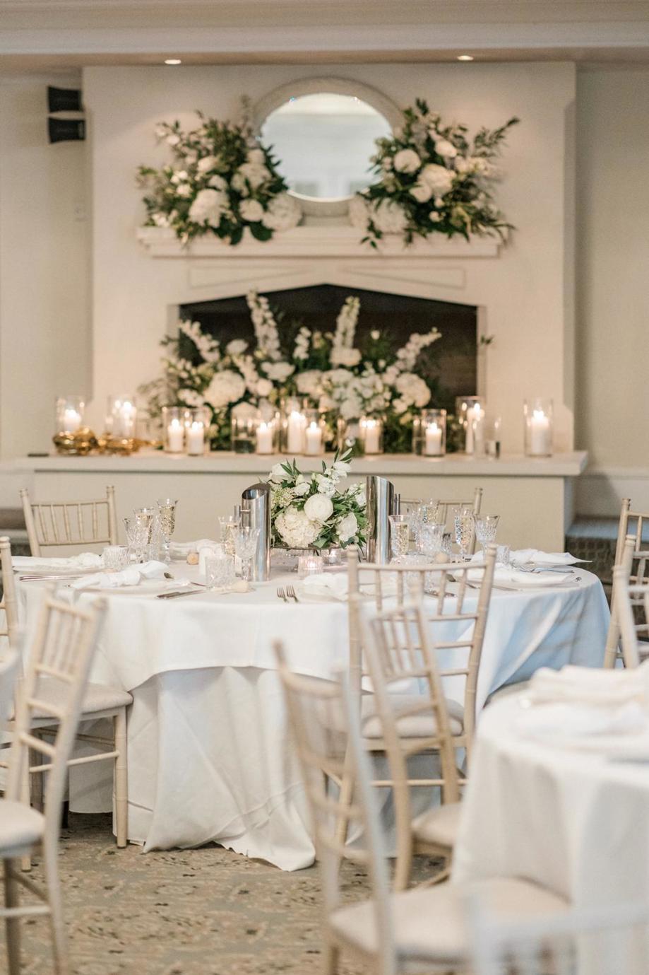 Large flower-decorated fireplace with tables set up for wedding meal